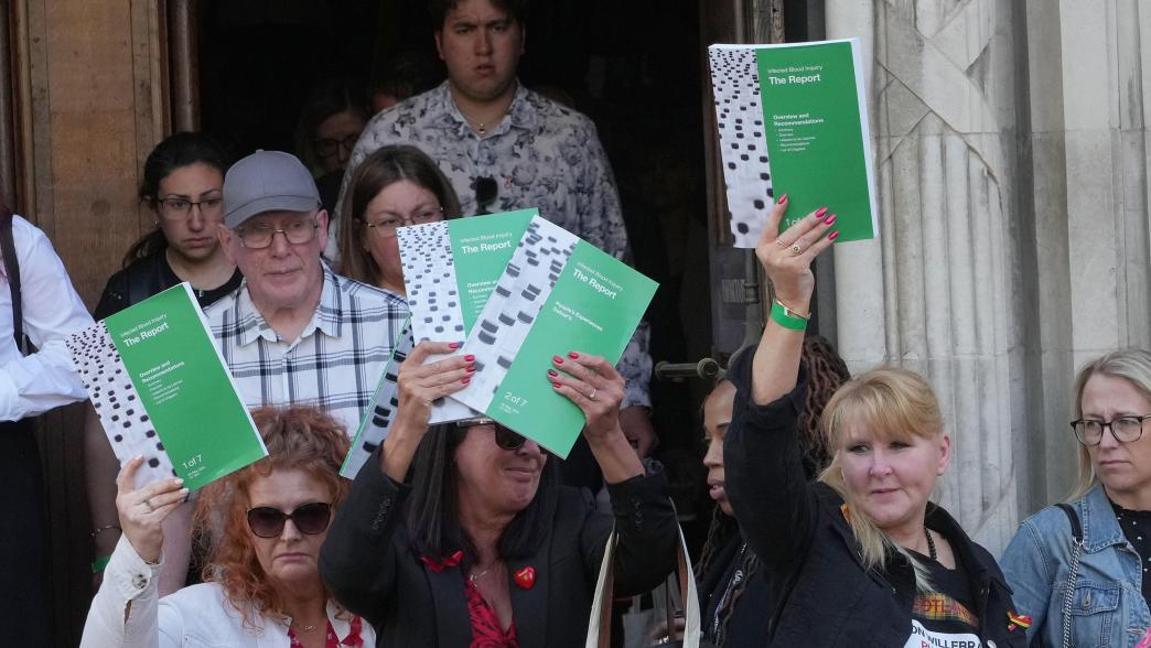 People hold up the Infected Blood Inquiry report outside Central Hall in Westminster, London, after it's publication. 